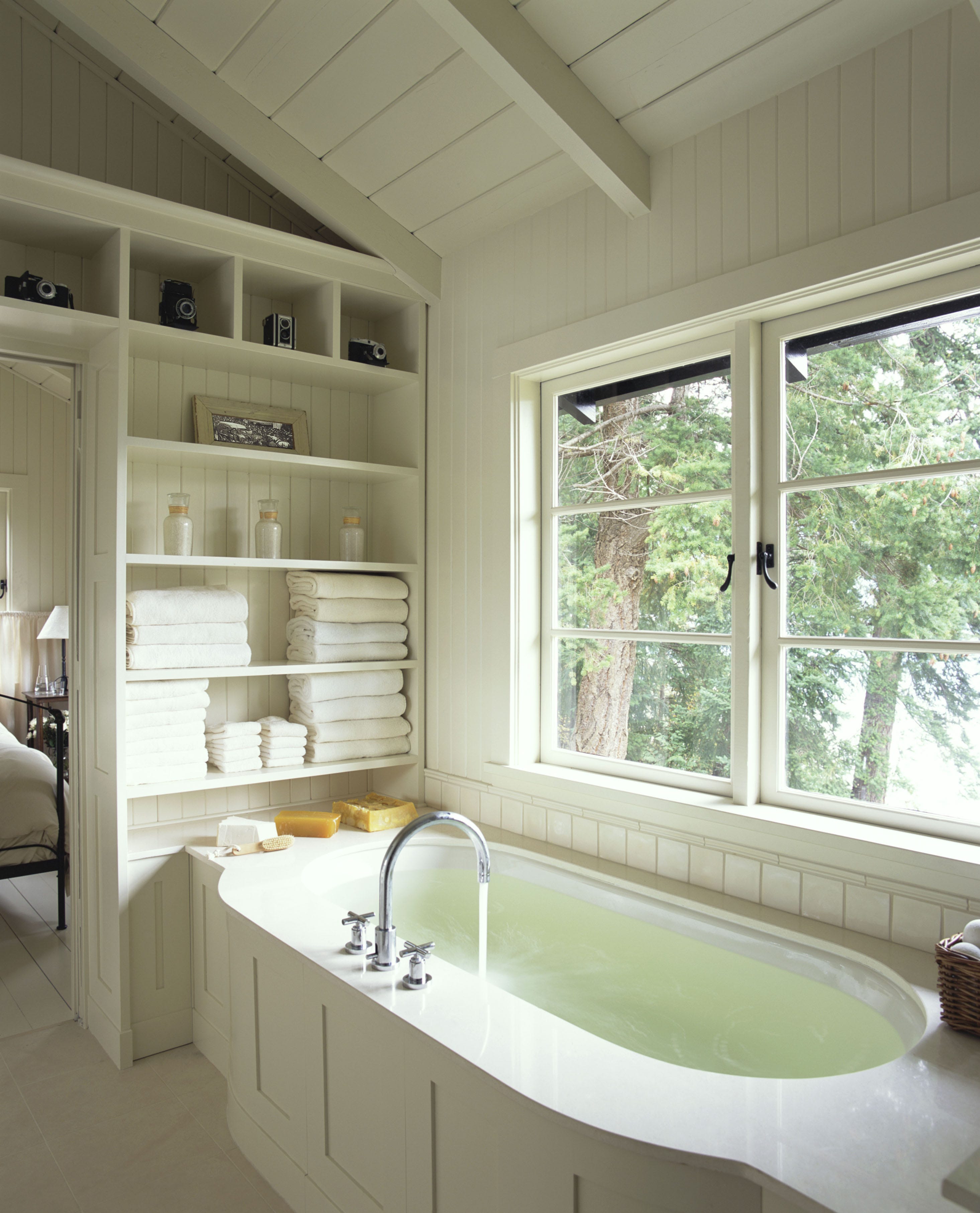 bathroom interior with a large white tub, built in shelves, and a view towards some trees